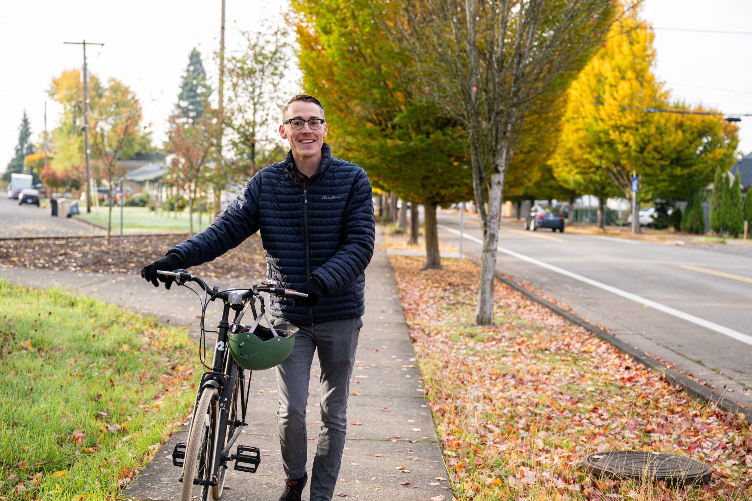 A man walking a bike on a suburban sidewalk, smiling.