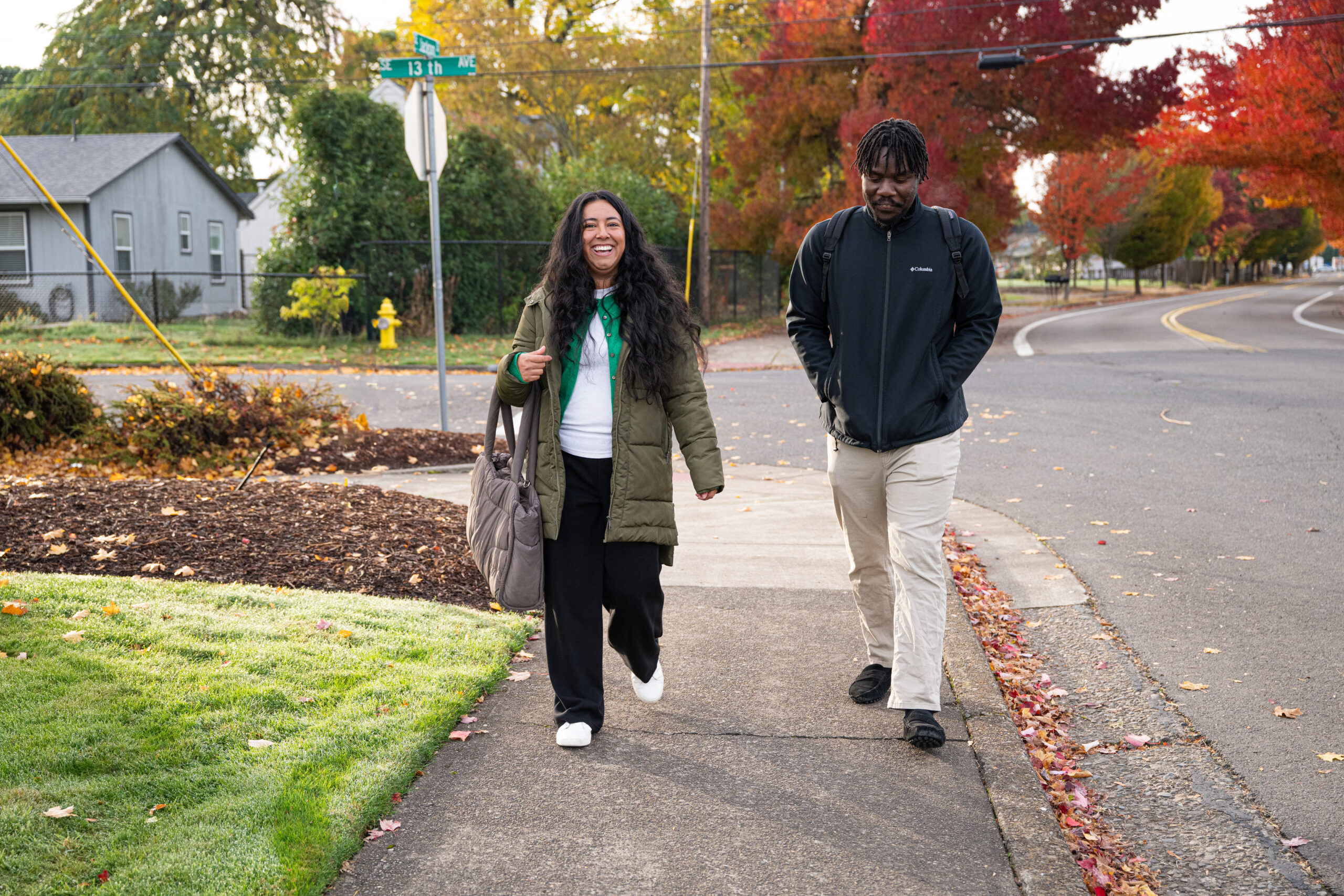 Two people walking down a neighborhood sidewalk in the fall.