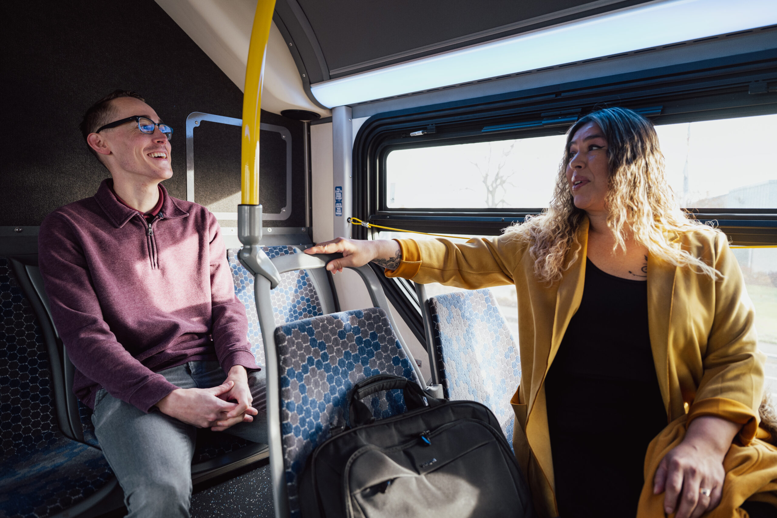 Two people on a public transit bus, smiling.