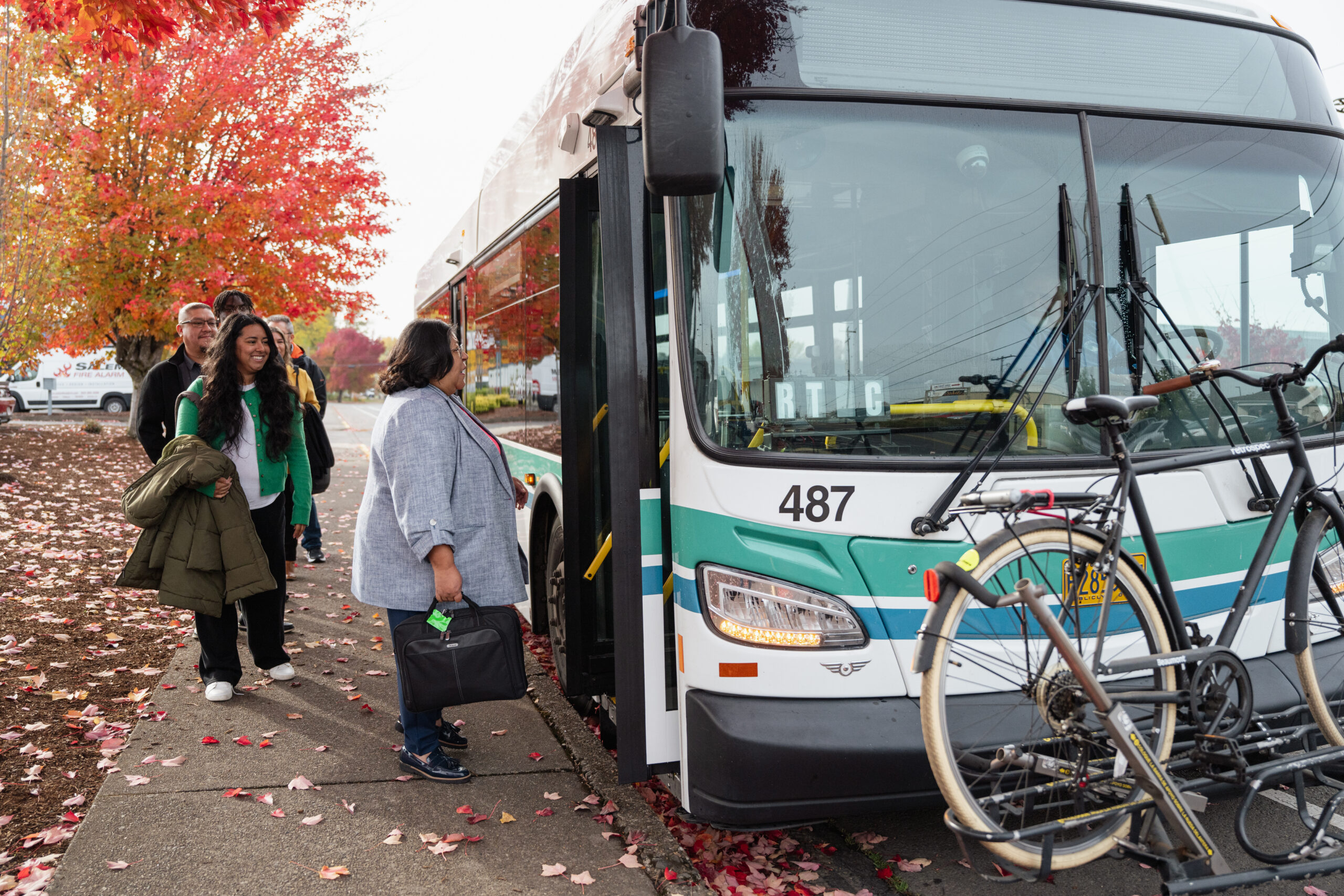 People boarding a transit bus in the fall near colorful leaves.