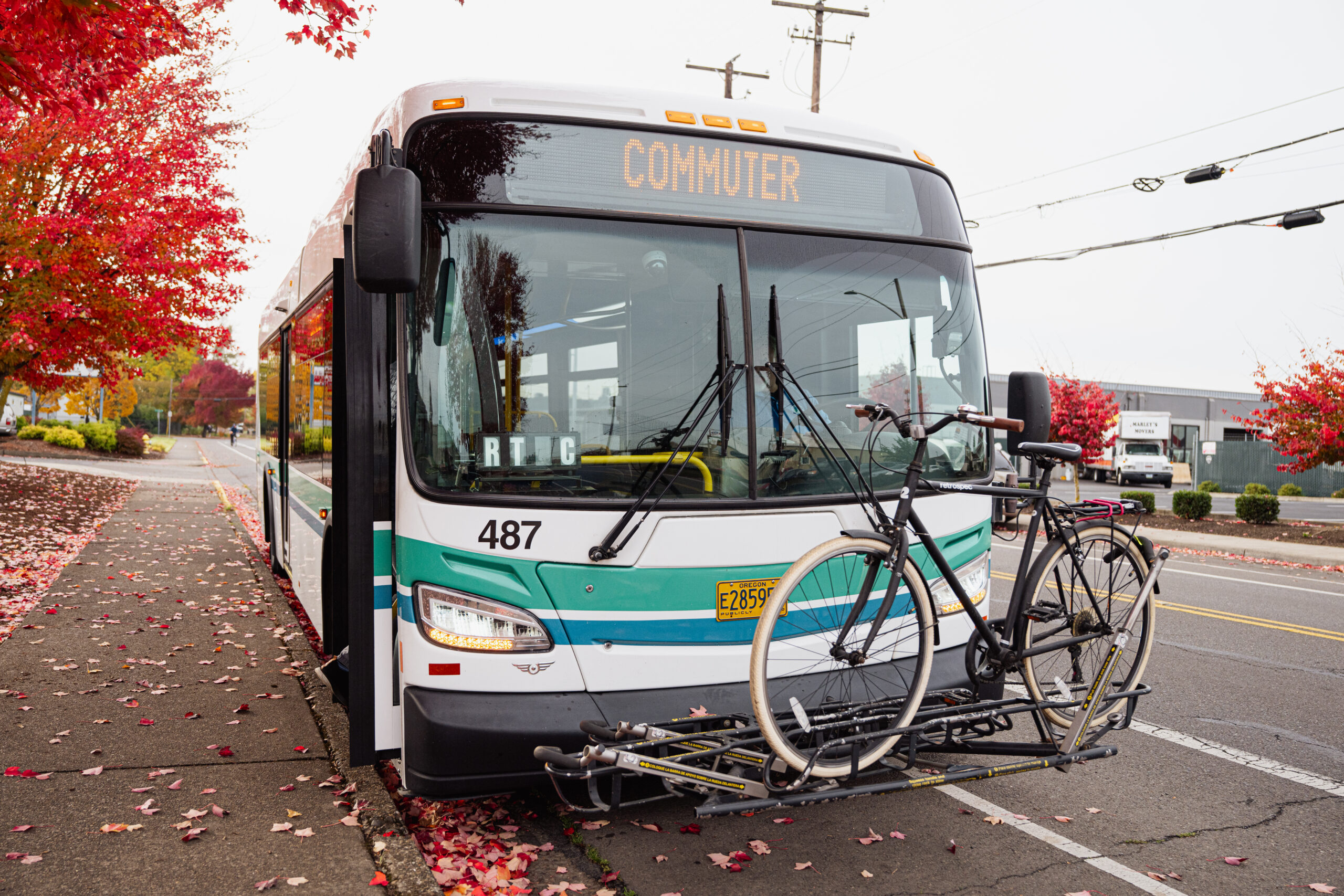 A bus surrounded by fall foliage with a bike mounted to the front, displaying the route text "Commuter."