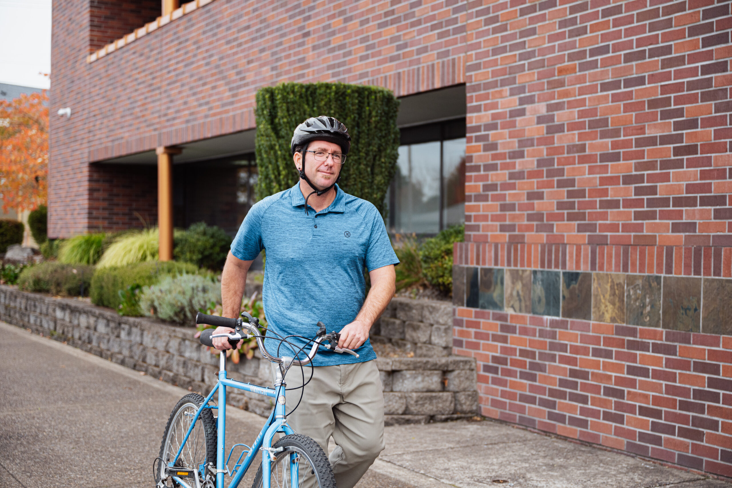 Man walking bike alongside a brick building.