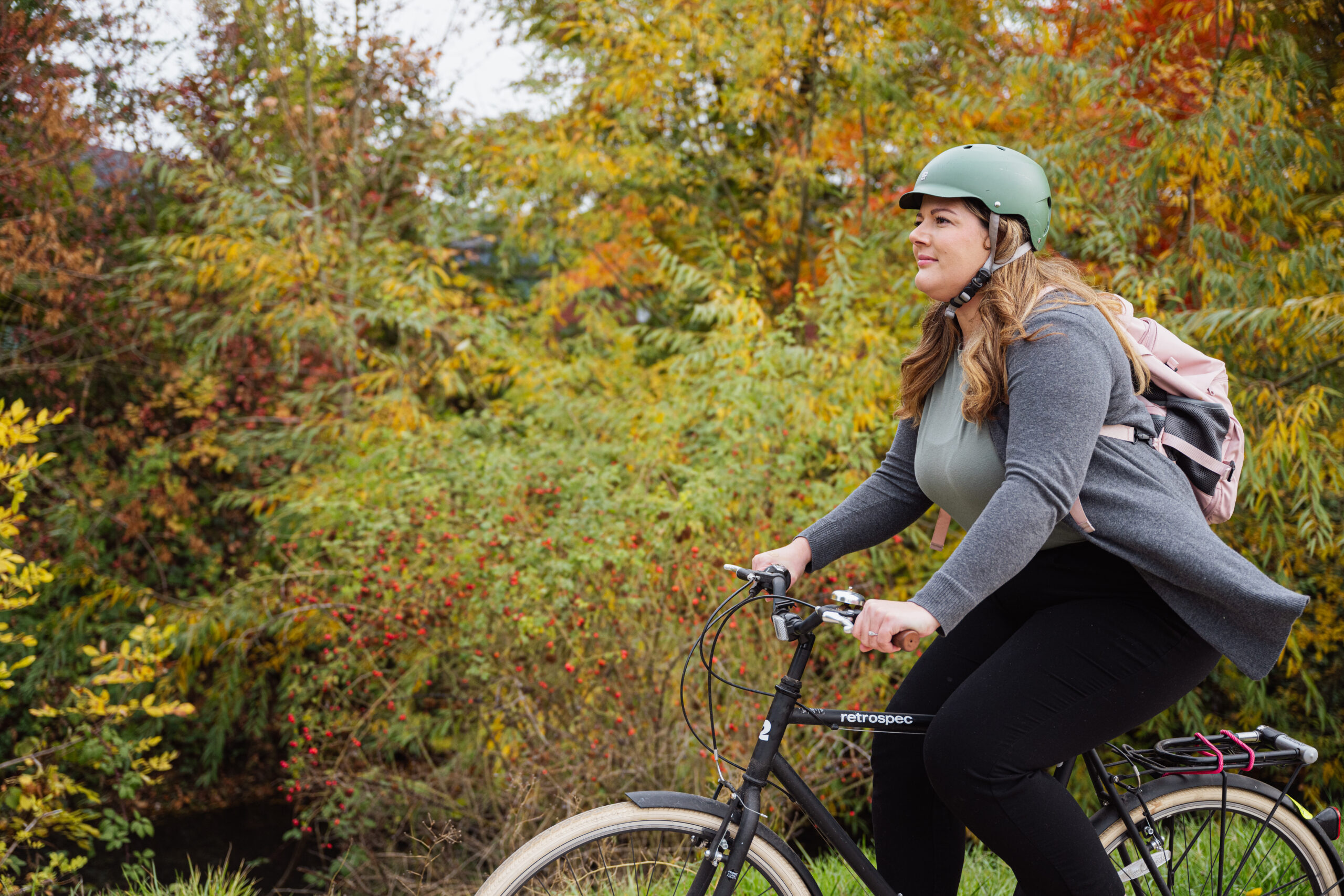 Woman biking in front of autumnal trees.