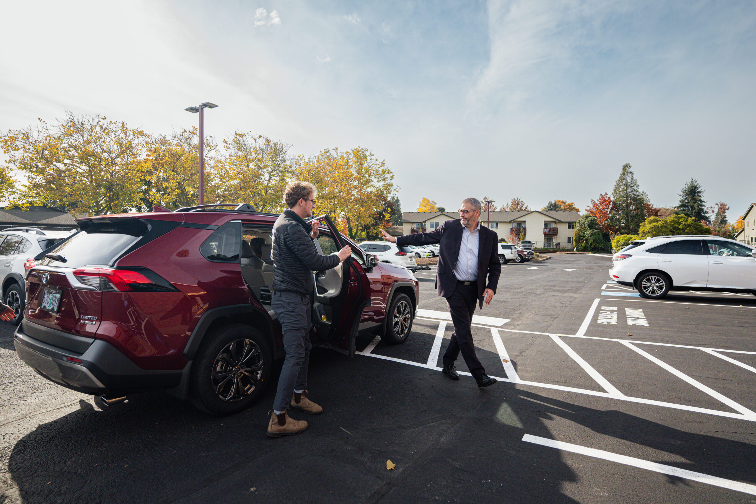 Two people exiting a parked car in a parking lot.