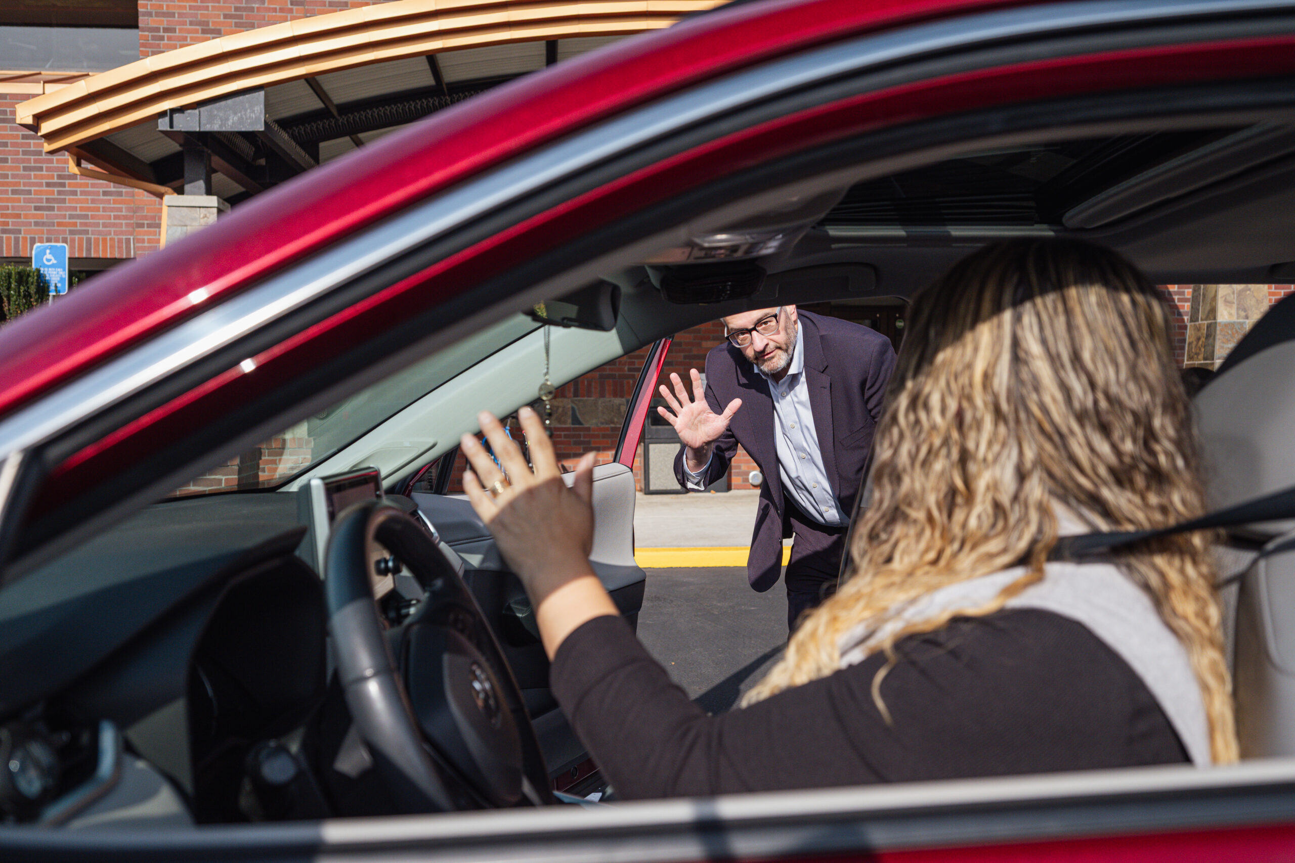 A passenger exiting a car while waving to the driver.