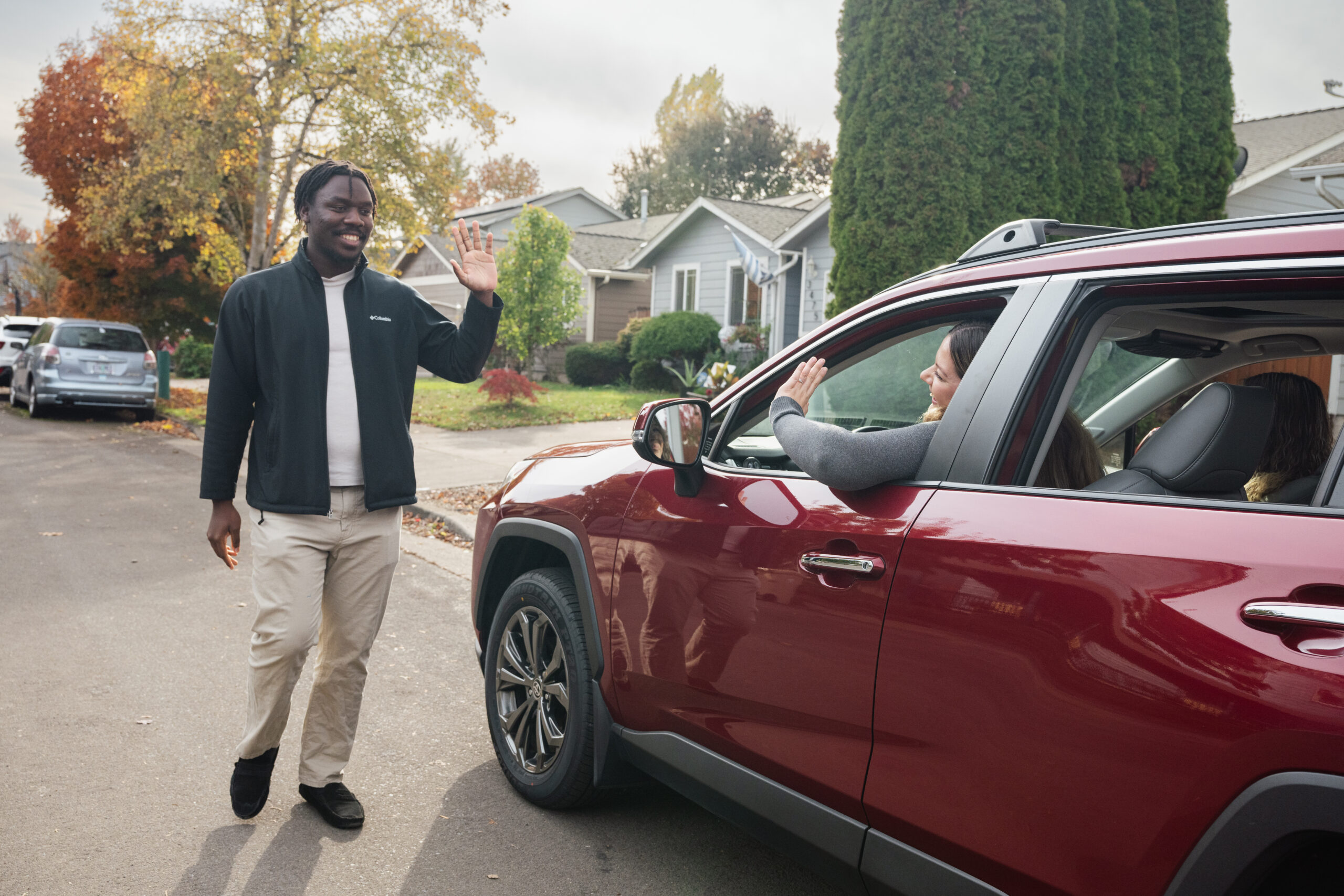 A person smiling and waving to the driver of a car while approaching.