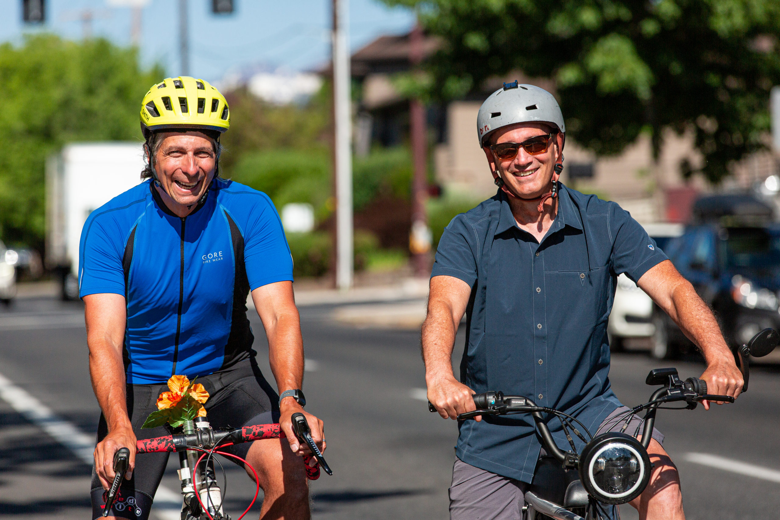 Two men biking on a street side by side and smiling.