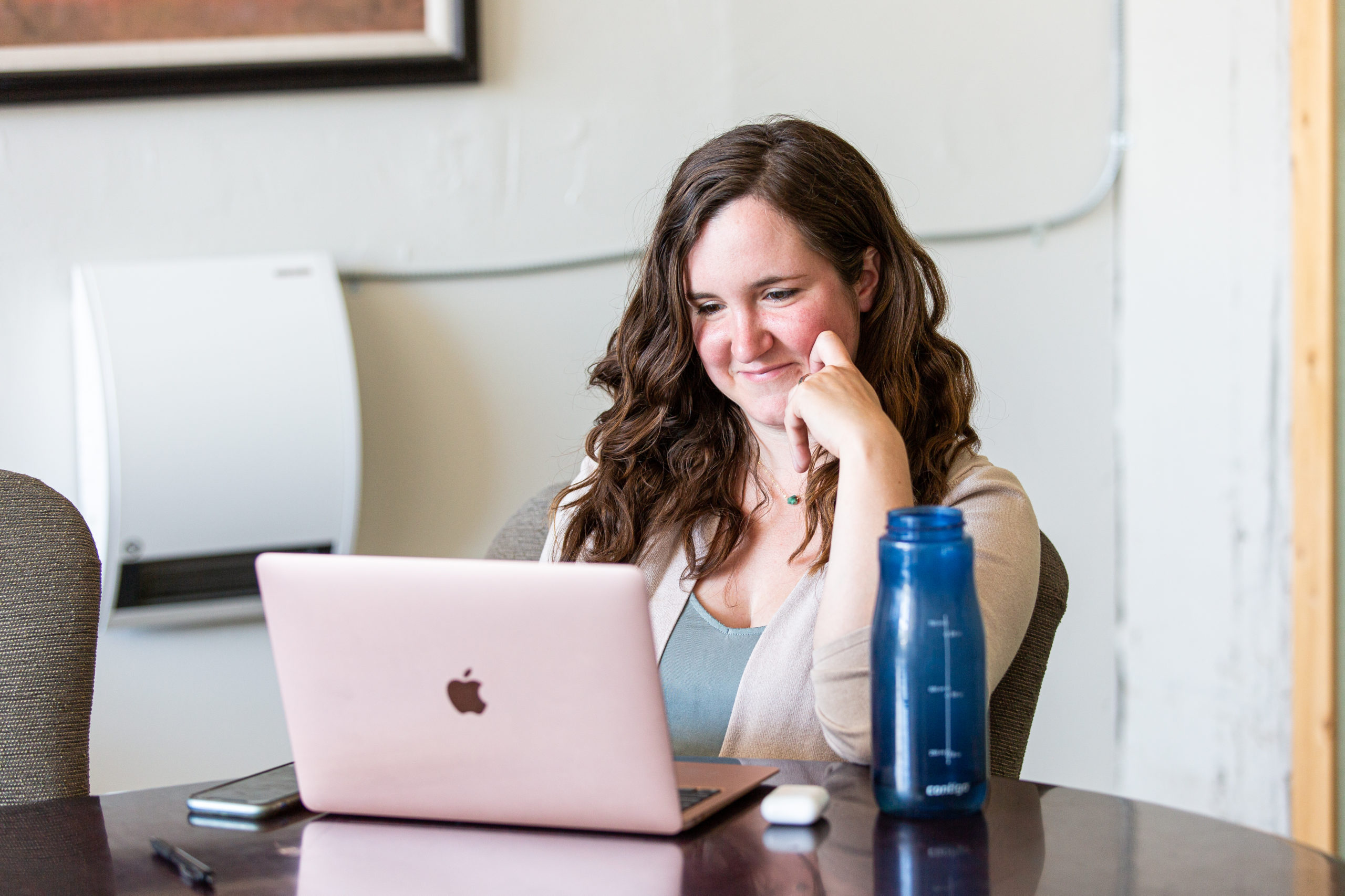 Woman smiling at a pink laptop.