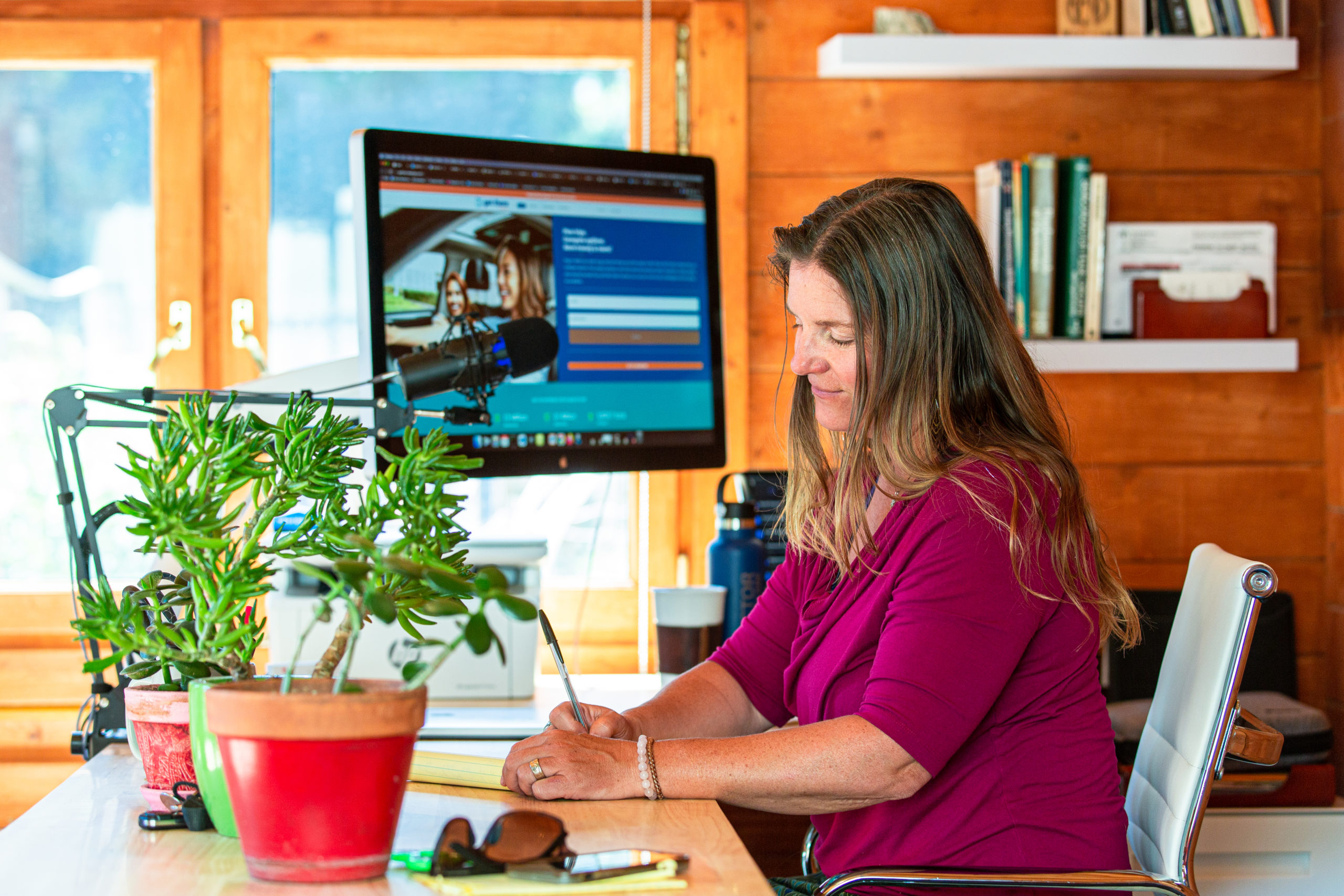 Woman seated at home desk taking notes.
