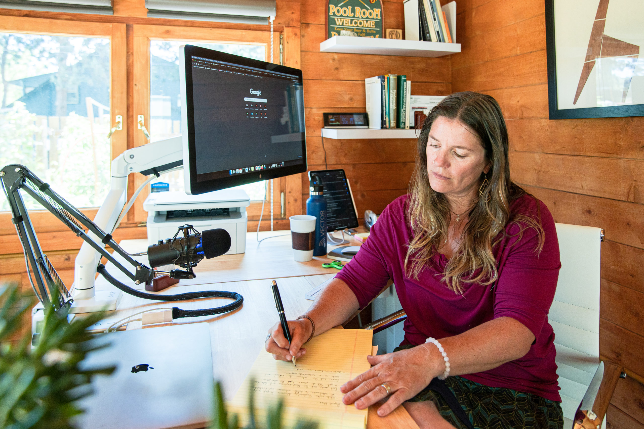 Woman seated at home desk writing on notepad.