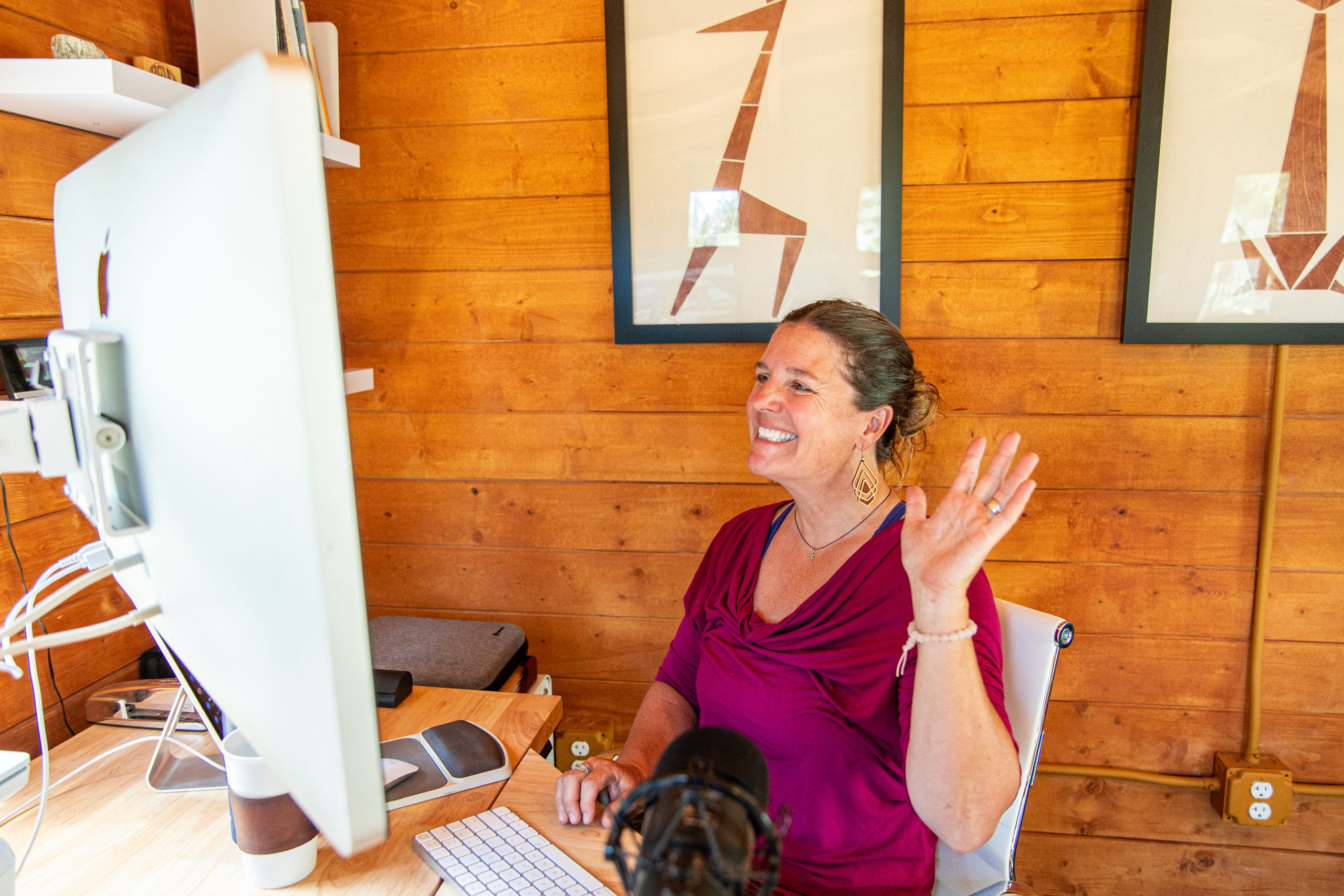 Woman seated at desk and waving at computer screen.