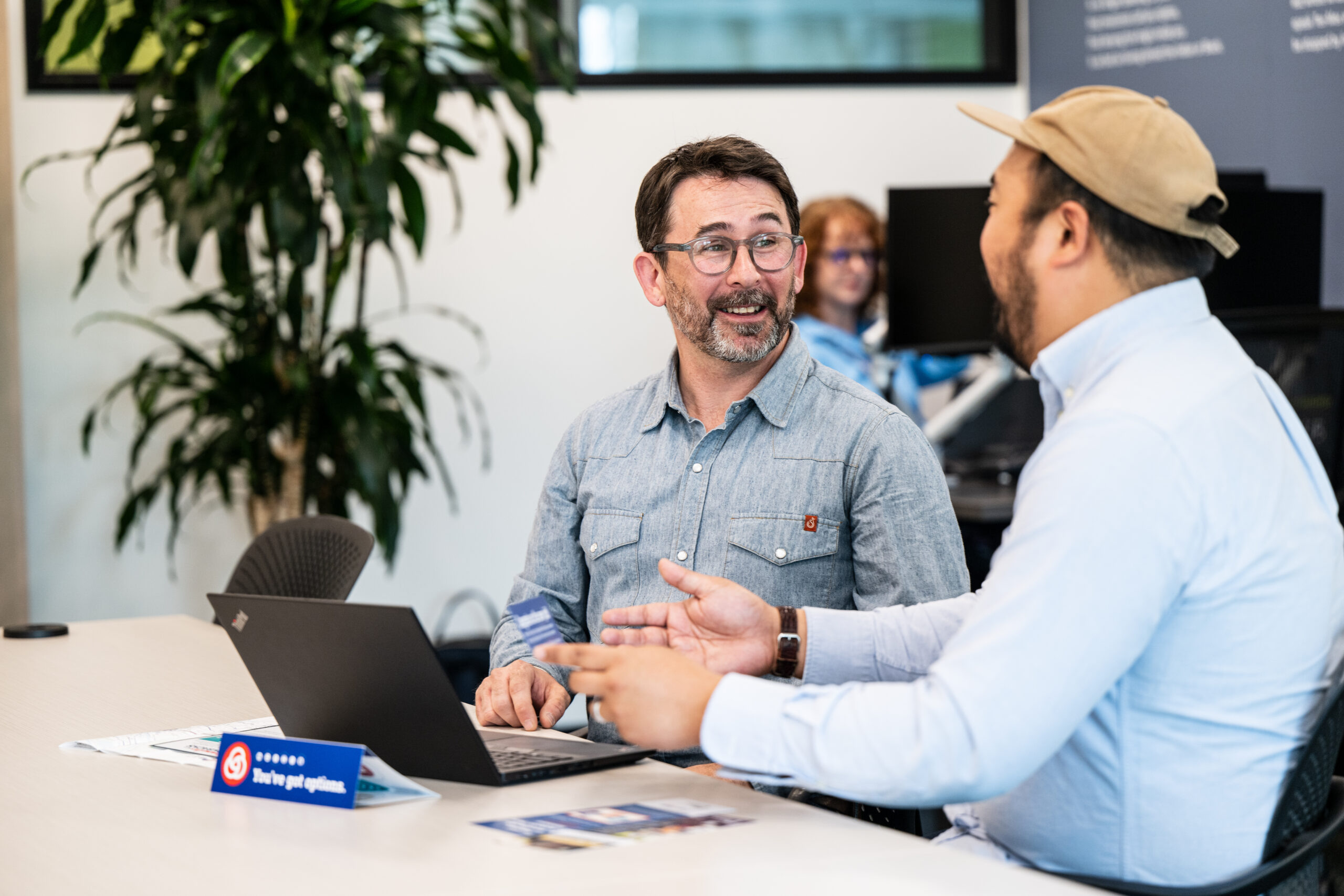 Two people smiling and talking by a laptop in an office setting.